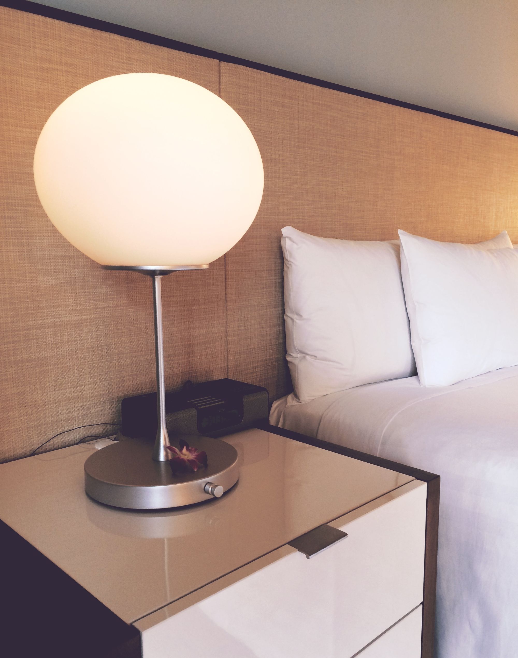 Freshly made hotel bed with white pillows beside a glowing bedside lamp