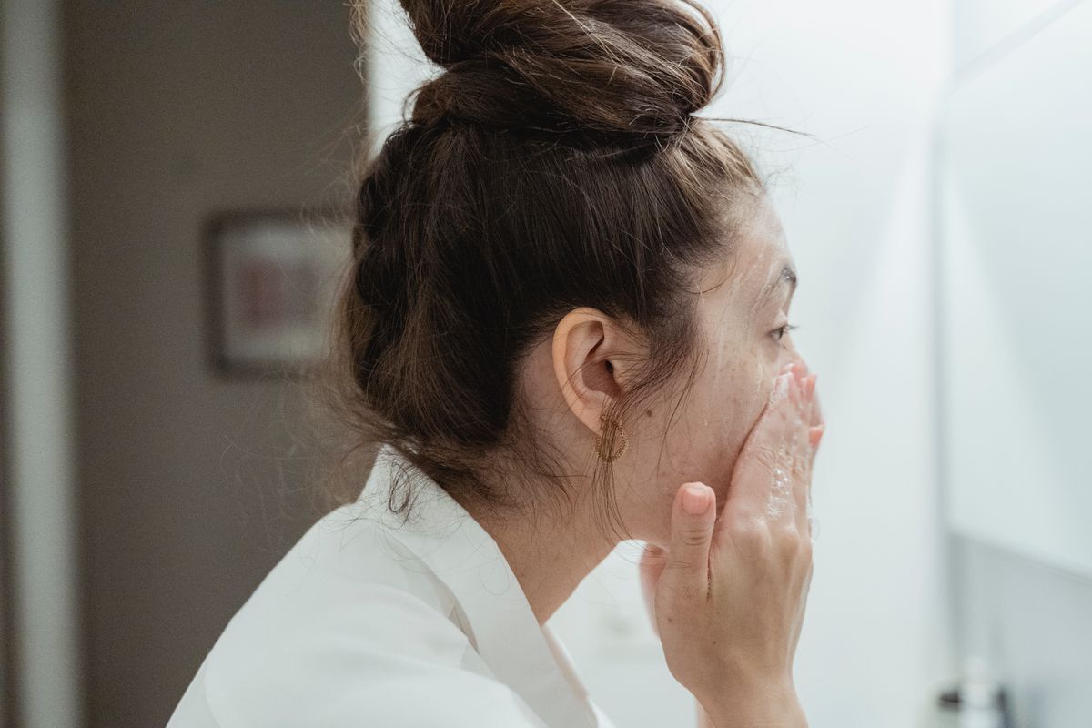 Guest in a white robe washing their face in a hotel bathroom